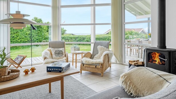 A spacious room with large windows, a fireplace, wicker furniture, and a table with a book. - "Gedda" -  from the sea by Interhome (Vestervig)