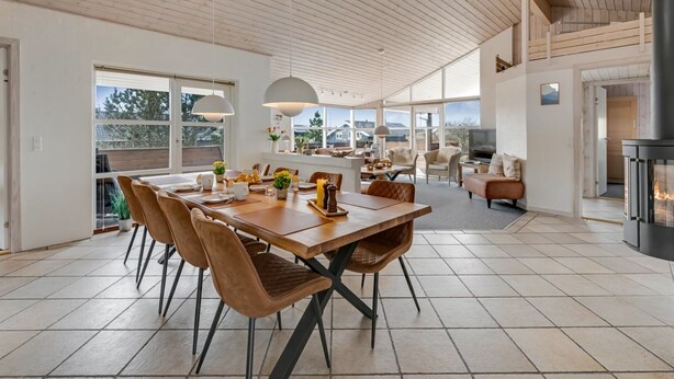 A spacious dining area with a wooden table and chairs, a fireplace, and large windows offering a view of the outdoors.