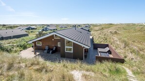 A modern house with a deck, surrounded by dunes and other houses.