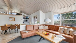 A modern living room with a sofa, coffee table, and dining area with chairs and a TV.
