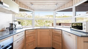 A compact kitchen with wooden cabinets, a built-in oven, a microwave, and a large window offering a view of the beach.