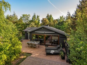 Eine moderne Hütte mit einer Terrasse, Sitzgelegenheiten im Freien und einem großen Schiebeglastür.