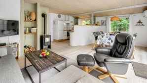Een moderne woonkamer met een open haard, een eethoek met een tafel en stoelen, een keuken met een koelkast en fornuis, en een tv aan de muur bevestigd.