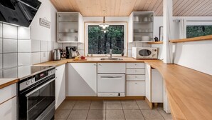 Een moderne keuken met witte kastjes, een houten aanrecht, een ingebouwde oven, een magnetron en een raam met uitzicht op bomen.