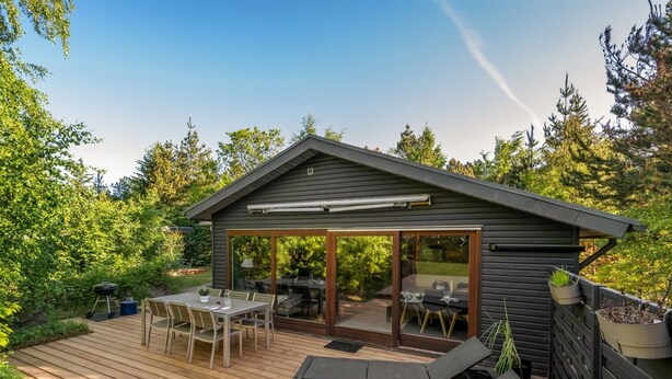 Een houten terras met buitenmeubilair, een overdekte patio en een klein gebouw met een glazen deur.