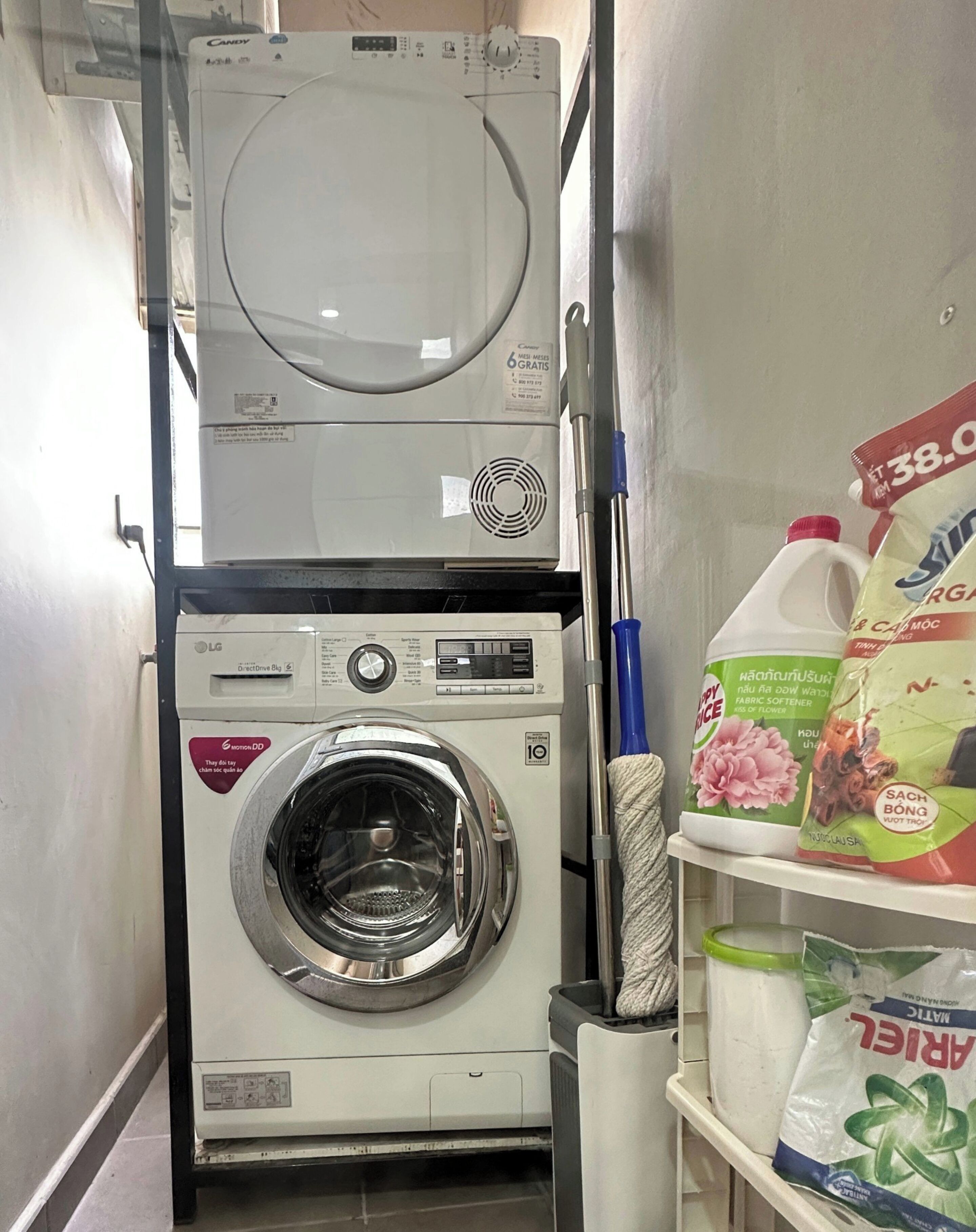 A laundry area with a stacked washer and dryer, a mop, and bags of laundry detergent.