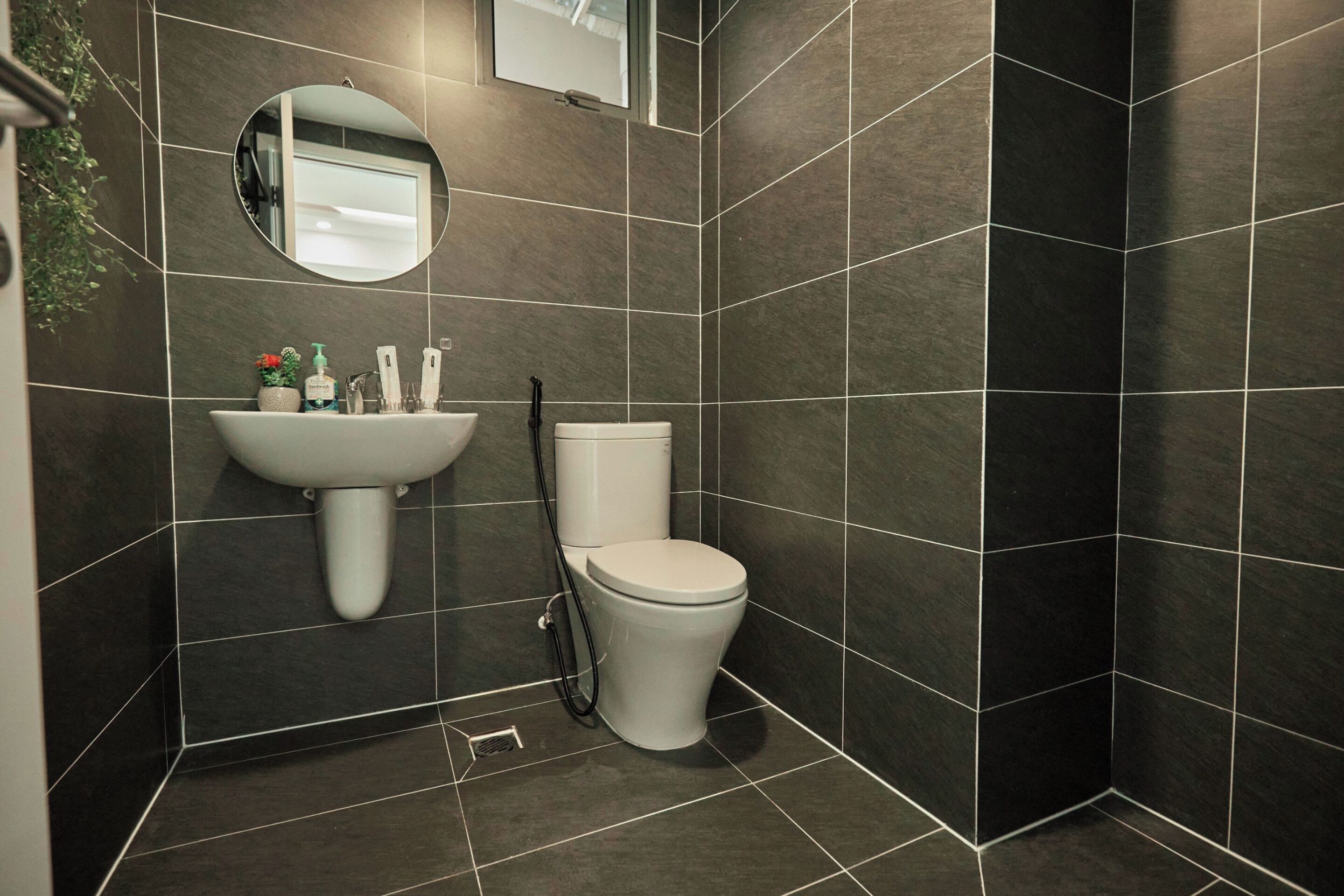 Un baño con baldosas oscuras, un lavabo blanco, un inodoro y un espejo.