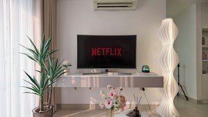 A modern living room with a flat-screen TV displaying "NETFLIX," a potted plant, a decorative vase, and a unique white lamp. - The MASTERI ANGIA Prestige Suite By An Gia Hospitality (Ho Chi Minh City)