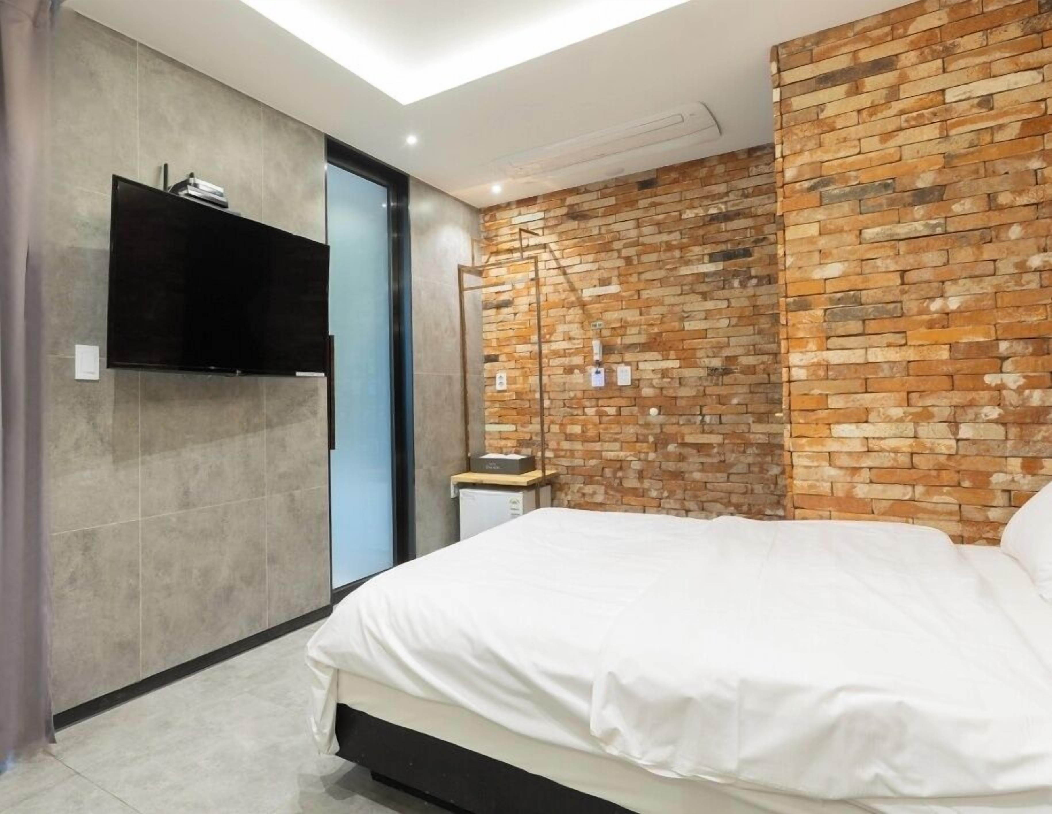 Une chambre moderne avec un mur d’accent en briques, un téléviseur à écran plat et un design minimaliste.