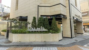 A hotel entrance with a sign reading "Des arts HOTEL" and a small garden area with potted plants. - Hotel Des Arts (Seoul)