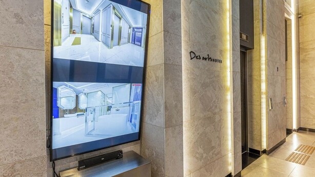 A digital display in a hotel lobby showing different areas of the hotel, including a reception area and a modern bathroom. - Hotel Des Arts (Seoul)