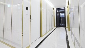 A corridor with white marble walls and doors, a black and gold striped floor, and a door with a sign reading "101". - Hotel Des Arts (Seoul)