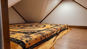 A bedroom with a sloped ceiling, a bed with a patterned bedspread, and wooden flooring.