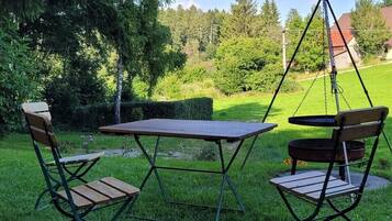 Eine Terrasse mit Tisch und Stühlen, umgeben von Rasen und Bäumen.