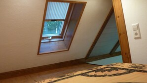 A room with a sloped ceiling, a small window, a wooden beam, and a power outlet.