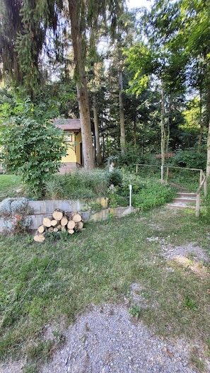 Eine rustikale Holzhütte, umgeben von dichtem Wald, ein Kiesweg führt zu einer Holztreppe, und ein Holzstoß liegt bereit.
