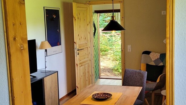 A room with a wooden table, a chair, a television, and a door leading outside.
