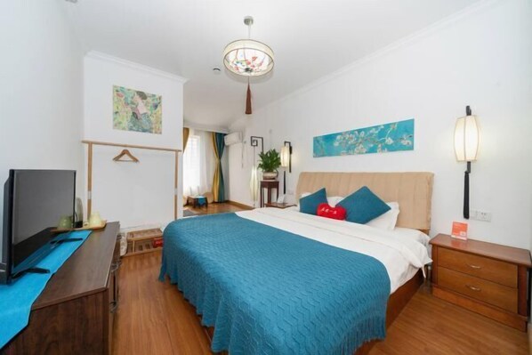 Une chambre d’hôtel équipée d’un lit, d’une table de chevet, d’une télévision et décorée avec des œuvres d’art aux murs.