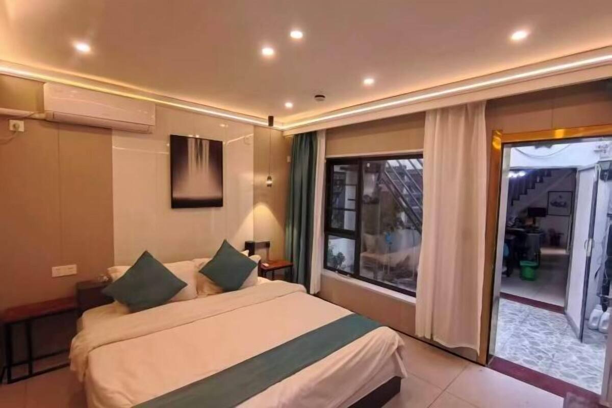 A hotel room with a bed, a TV, a window, and an air conditioning unit.