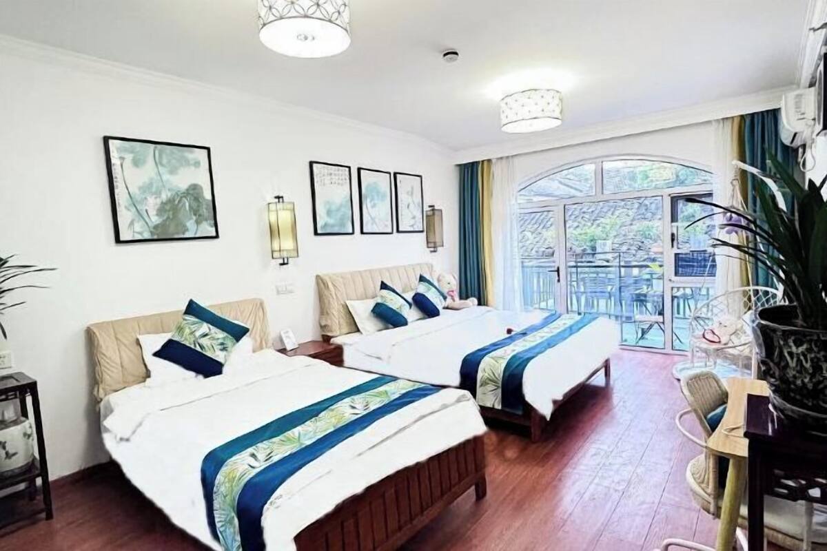 A hotel room with two beds, a large window with a view, and a dining area with chairs.