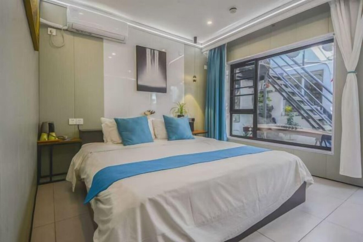 Une chambre d’hôtel avec un grand lit, une fenêtre donnant sur un escalier extérieur et un climatiseur fixé au mur.