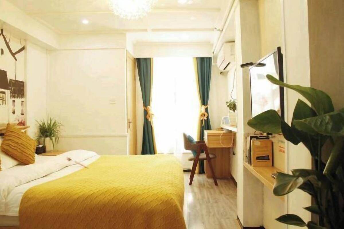 A hotel room with a bed, desk, chair, and large windows with curtains.