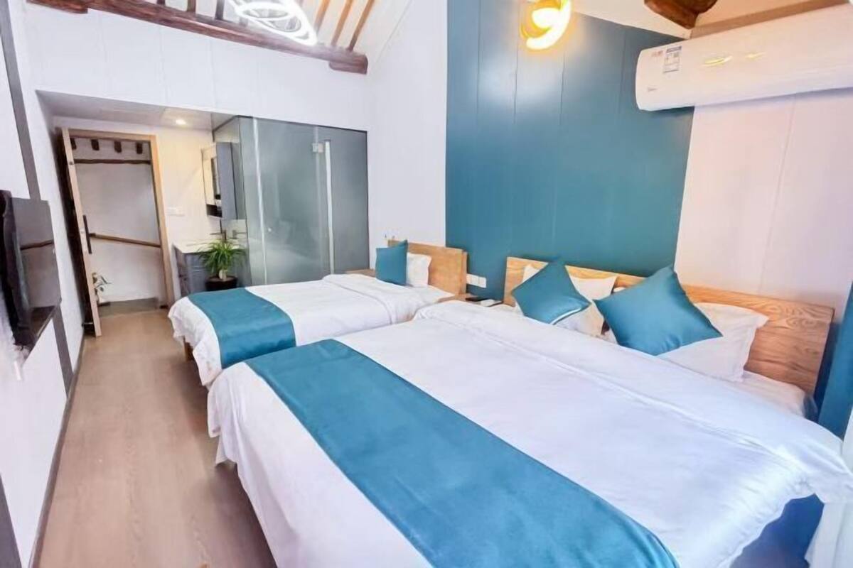 A hotel room with two beds, a kitchenette, a ceiling fan, and a large window.