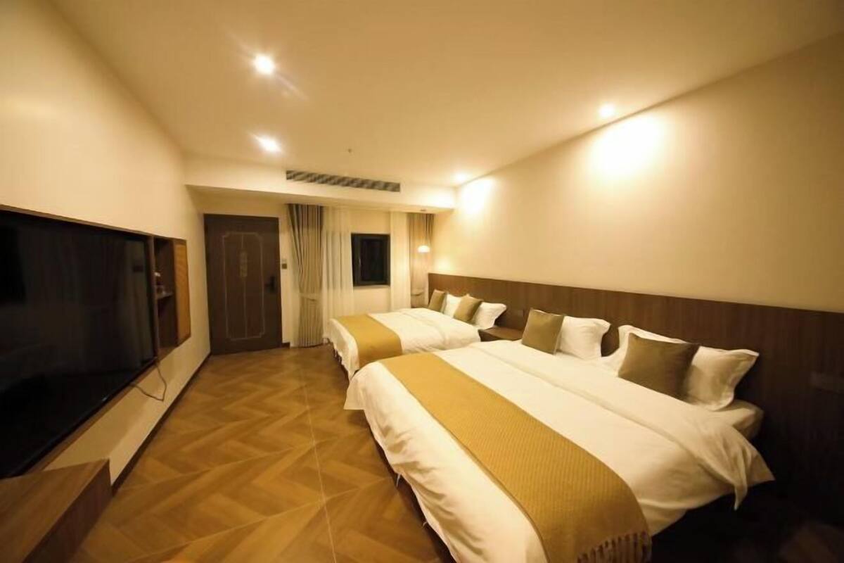 A hotel room with two beds, a television, and a wooden floor.