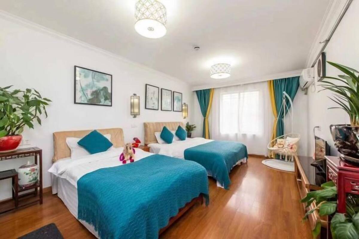 A hotel room with two beds, a wooden floor, a small table with a plant, and a window with curtains.