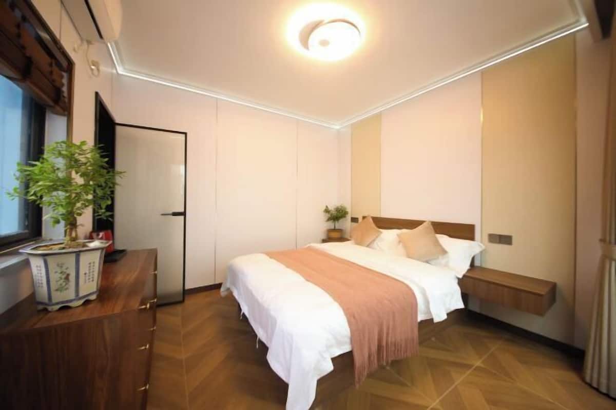 A hotel room with a bed, bedside table, potted plant, and a window.