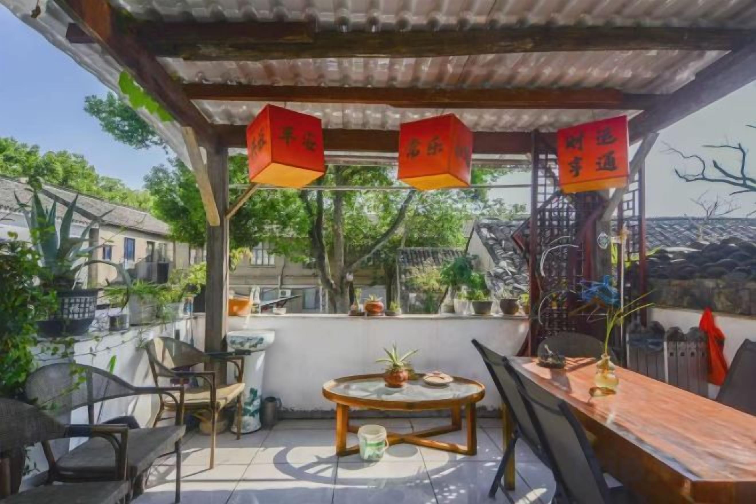 A covered outdoor seating area with tables and chairs, a small round table with a plant, and hanging lanterns.