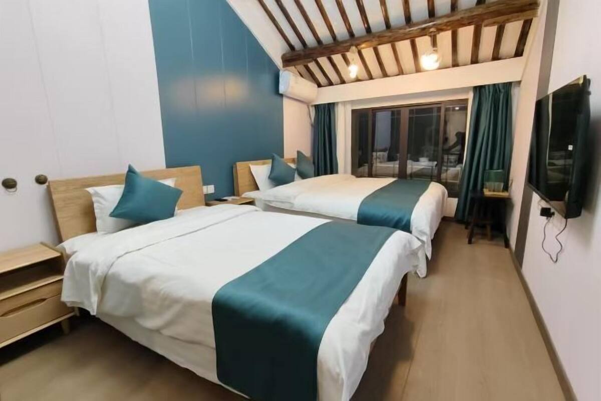 A hotel room with two beds, wooden headboards, a TV, and a balcony with a view.