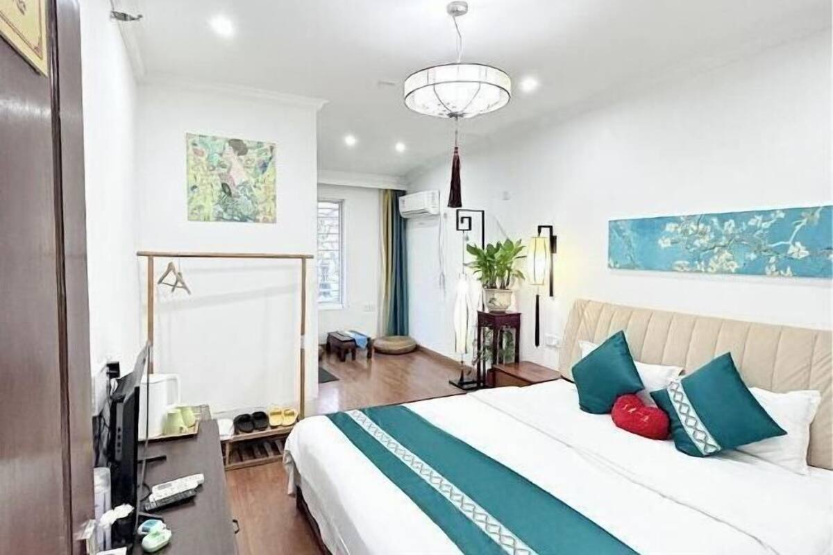 A hotel room with a bed, a desk, a chair, a plant, and artwork on the walls.