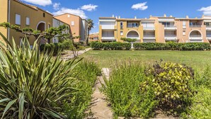 Un patio con un sendero que conduce a un edificio con varios balcones y un cielo azul despejado.