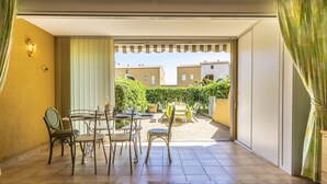 Un patio iluminado por el sol con una mesa y sillas, vistas de edificios al fondo y una puerta que da a un espacio al aire libre.
