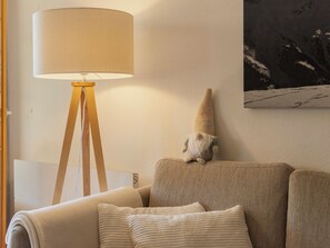 Ein Raum mit einer Lampe auf einem Dreibeinstativ, einer Couch mit Kissen und einem an der Wand hängenden Bild.