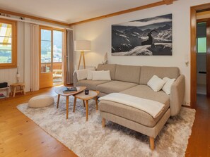 A cozy living room with a sofa, a small table, a lamp, and a painting of mountains.