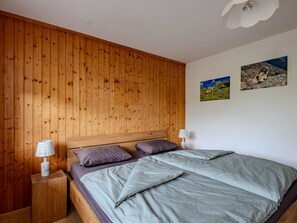 Ein Schlafzimmer mit einem hölzernen Kopfteil, zwei Kissen, einer Tagesdecke, einem Nachttisch mit Lampe und zwei Wandbildern.