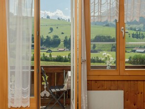 A room with a wooden interior, a view of a green landscape, and a small table with a chair.