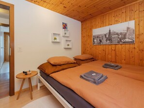 Une chambre avec un plafond en bois, un lit avec une literie orange, une affiche représentant un paysage urbain et une petite table sur laquelle se trouve un jouet.