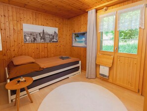 A wooden room with a bed, a small table, a heater, and a window with curtains. - Chalet Anita by Interhome (Zweisimmen)