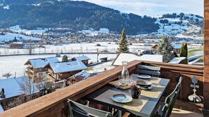 Eine Holzdar Terrasse mit Essplatz, mit Blick auf ein verschneites Dorf und Berge.