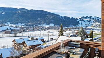 Eine Holzdar Terrasse mit Essplatz, mit Blick auf ein verschneites Dorf und Berge.