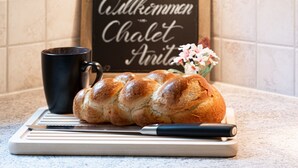 Ein Brotlaib auf einem Schneidebrett mit einem Messer, eine schwarze Tasse und ein Schild mit Herzen und Text im Hintergrund.