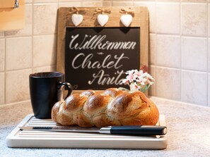 A loaf of bread on a cutting board with a knife, a black mug, and a sign with hearts and text in the background.