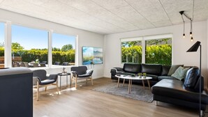Un salón amplio con un gran ventanal, un sofá de cuero negro, una mesa de centro y un televisor.