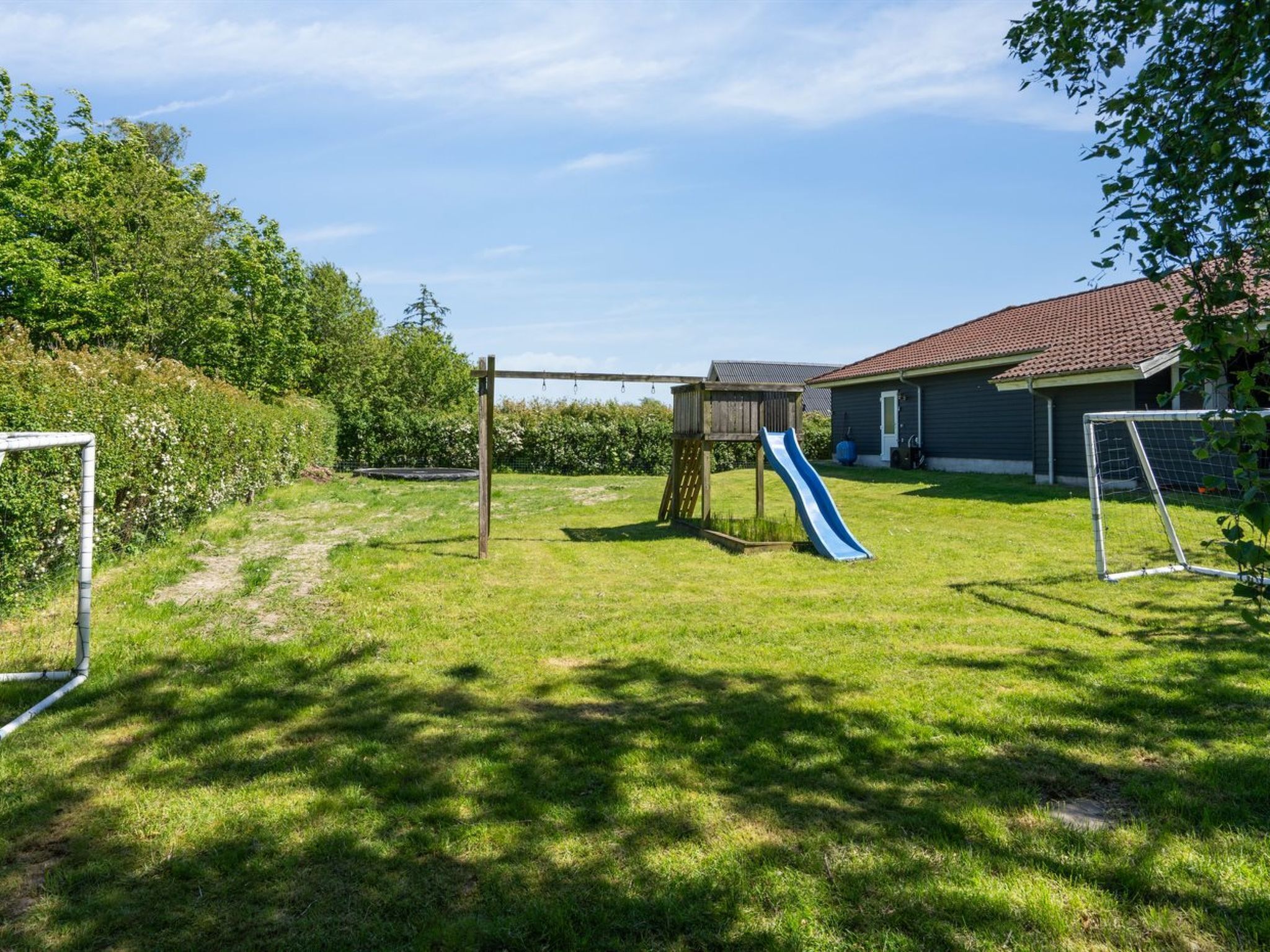 Un jardin avec une balançoire en bois, un toboggan bleu et un but de football.