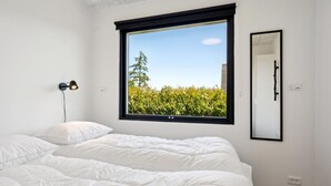 Un dormitorio con un ventanal grande, una cama, una lámpara de noche y un espejo.