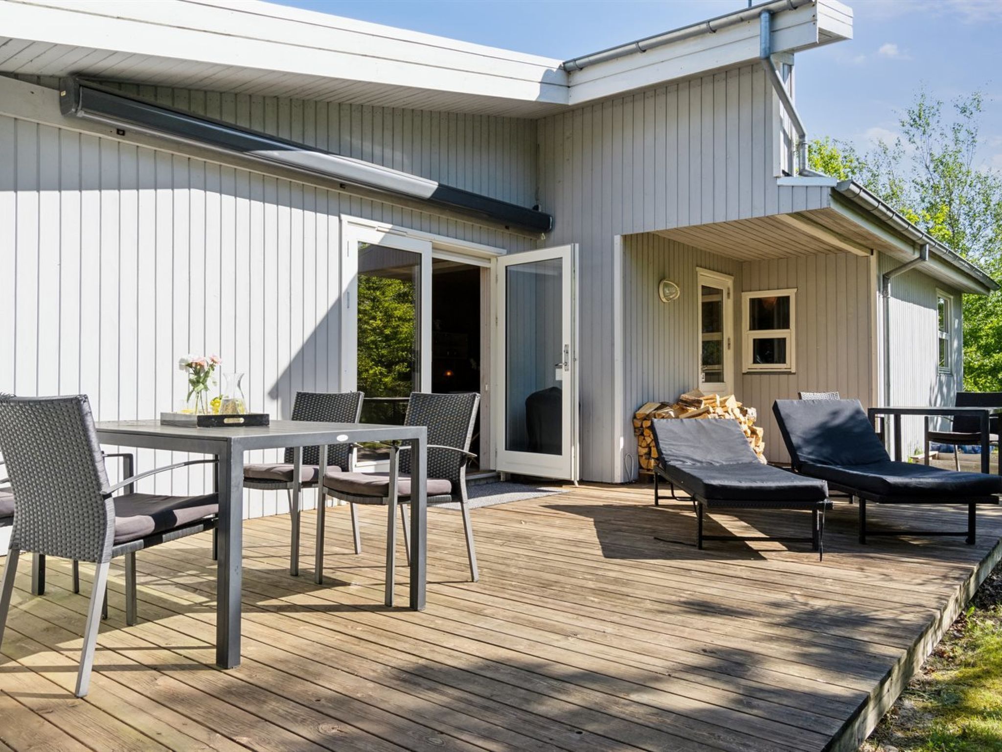 A modern outdoor deck with a table and chairs, a covered seating area, and a sliding glass door leading to a covered patio.