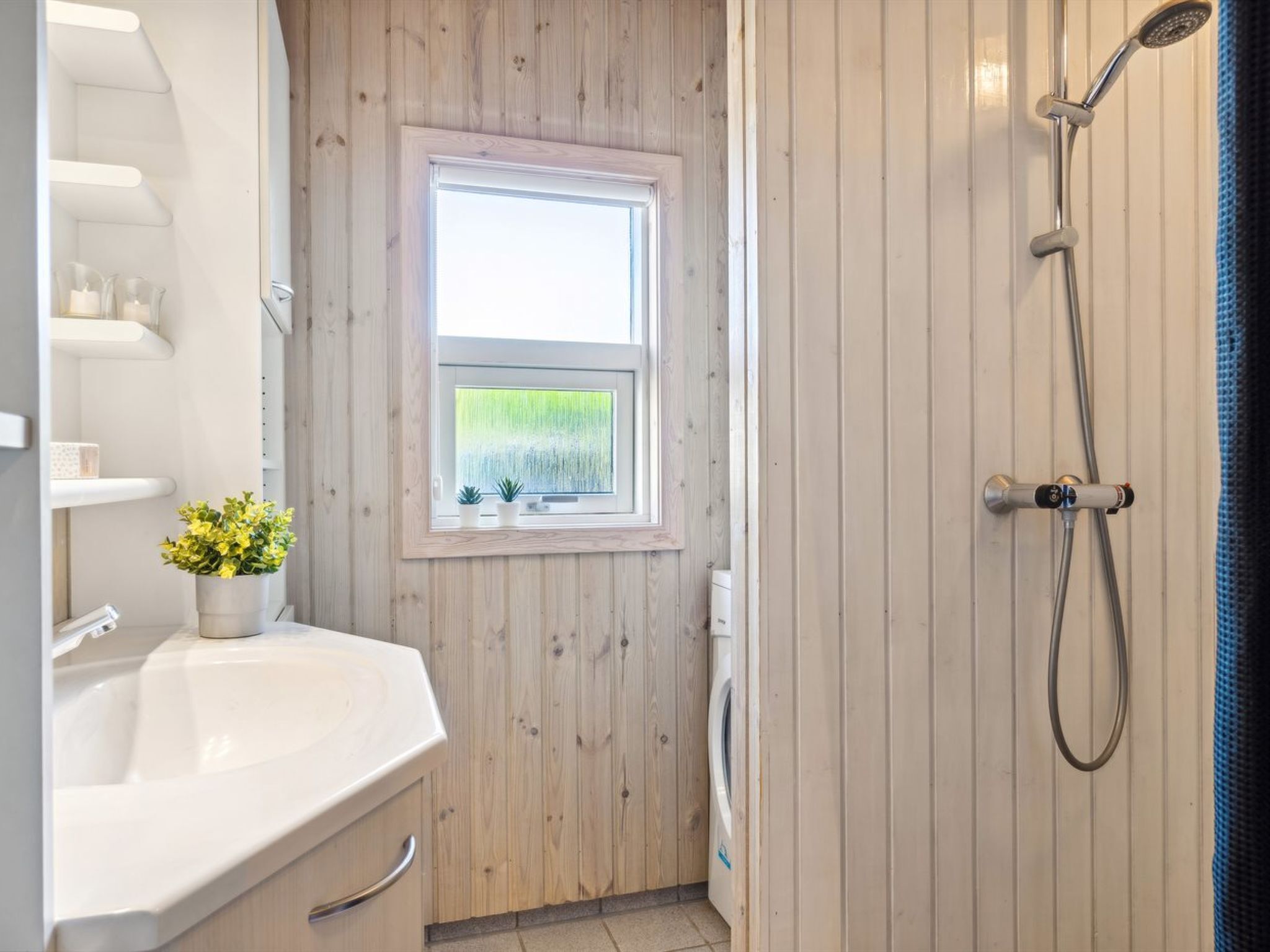 A bathroom with a wooden wall, a window, a shower, and a sink with a potted plant.